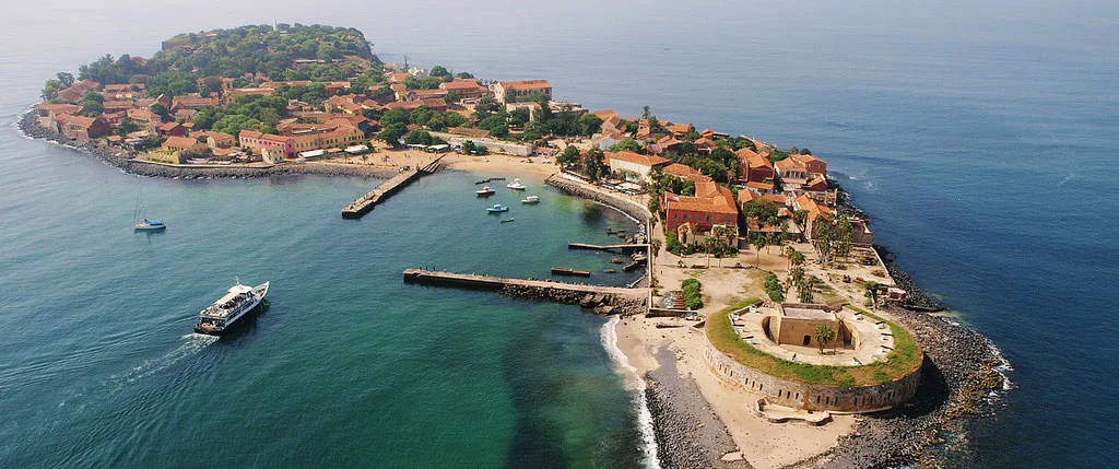Île de Gorée : vue sur les maisons ocre et rouges de l'île, son petit port et les pirogues sur une mer turquoise au large de Dakar